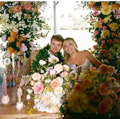 a man and woman sitting next to each other in front of floral arrangements on a table