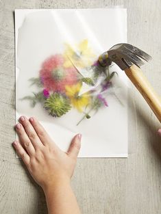 someone is painting flowers on a piece of paper with a paintbrush in their hand