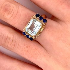 Vintage 1940's 10k yellow gold blue rectangular stone ring. The ring has three round dark blue stones on each side. The size of the ring is a 6.75, and has the ability to be resized. The height of the ring off of the finger is 7.5mm. The width of the band is 3.5mm, and tapers down to 2.1mm. Rectangular Sapphire Ring With Prong Setting, Blue Emerald Cut 14k Gold Sapphire Ring, 14k Gold Blue Three Stone Jewelry, Sapphire Rings With Prong Setting In Rectangular Shape, Blue Three Stone Emerald Cut Jewelry, Blue Emerald Cut Three Stone Jewelry, Blue Emerald-cut Three-stone Jewelry, Gold Rectangular Blue Topaz Rings, Rectangular Blue Topaz Ring With Prong Setting