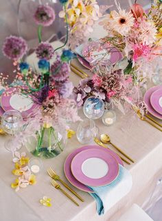 the table is set with pink plates and gold place settings, along with flowers in vases