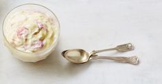 two spoons sitting next to a cup with food in it on a white surface