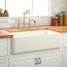 a white kitchen sink sitting under a window next to a counter top with spices on it