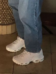 a person wearing white sneakers and jeans standing on tiled floor next to a toilet bowl