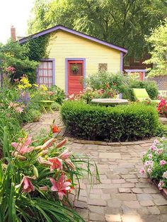 a small yellow house surrounded by flowers and bushes