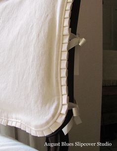 a white blanket hanging on the side of a black and white bed with ruffled edges