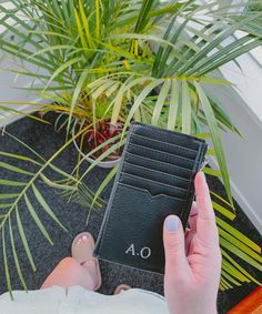 a person holding a black card case next to a potted plant