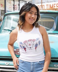 Get ready to show your inner cowboy with this classic and cool tank. Featuring a longhorn skull with red roses and feathers in blue and red. Show your wild side with bold American spirit and cinched side ties on a soft white fabric. Model is wearing a size small. 58% Cotton 38% Polyester 4% Spandex Imported Machine wash cold, with like colors No bleach Tumble dry low Low iron if Casual Tank Top For Summer Rodeo, Casual Sleeveless Tank Top For Rodeo, White Tops For Summer Rodeo, Western Style Sleeveless Tops For Spring, Fitted Sleeveless Top For Rodeo, White Summer Tops For Rodeo, Sleeveless Western Tops For Spring, White Top For Rodeo Summer Events, Western Style Sleeveless Tank Top For Rodeo