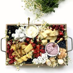 a platter filled with cheese, fruit and dips on a table next to flowers