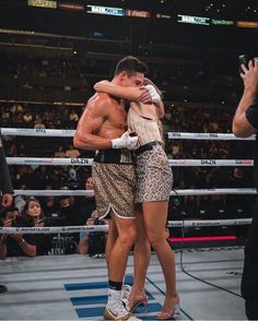 two men hugging each other in the middle of a boxing ring with people watching from the stands