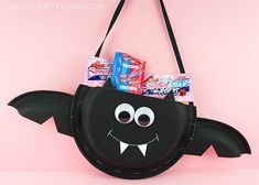 a paper plate bat with candy in it's mouth hanging from a string on a pink wall