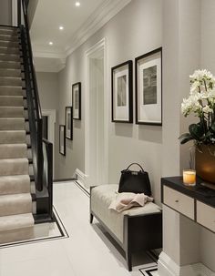 a white and black hallway with flowers on the table next to the stairs leading up to the second floor