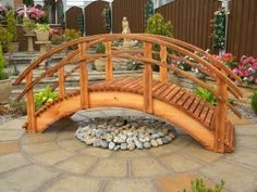 a wooden bridge over a small pond with rocks and plants around it in a garden