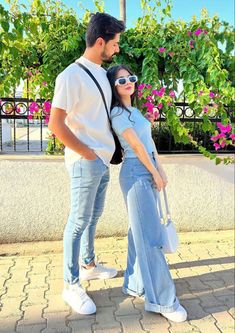 a man and woman standing next to each other in front of some pink flowered bushes