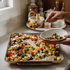 two hands reaching for a bowl of food on top of a baking sheet in a kitchen