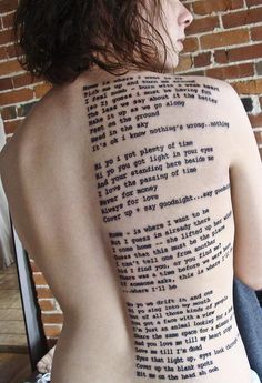 a person with a tattoo on their back that has words all over it and is sitting in front of a brick wall