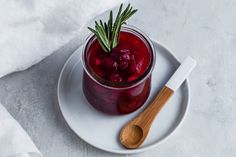 a small jar filled with cranberry sauce on a white plate next to a wooden spoon