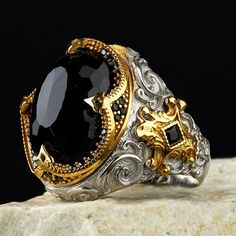 an ornately decorated ring with black stones and gold accents on top of a rock