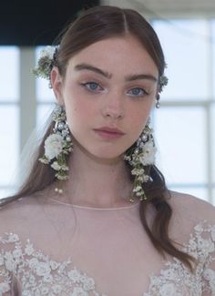 a woman with flowers in her hair wearing a wedding dress and earrings on her head