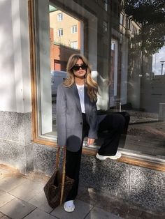 a woman standing in front of a window with her hand on her hip wearing sunglasses