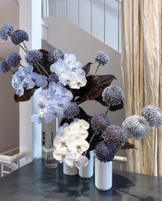 blue and white flowers sit in vases on a table next to a stair case