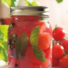 a jar filled with tomatoes and leaves on top of a table