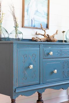 a blue painted dresser with flowers and vases sitting on it's sideboard