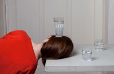 a woman leaning her head on a table next to two glasses and a blender