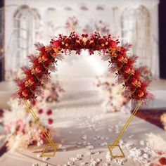 a wedding arch decorated with red flowers and gold stands in front of a white backdrop