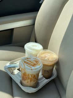 two cups of coffee sitting on a tray in the back seat of a car,