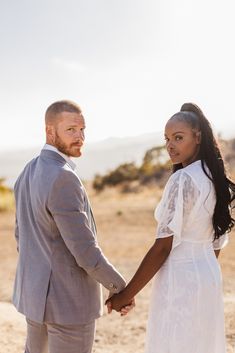 a man and woman are holding hands in the desert, looking into each other's eyes