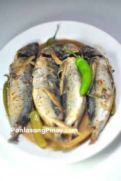 a white plate topped with fish covered in sauce and green peppers on top of it