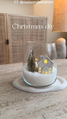 a small house in a glass bowl with snow on the bottom and christmas tree inside