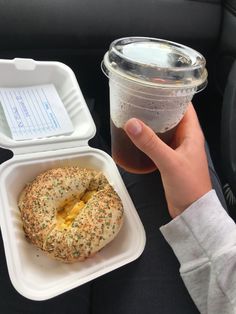 a person holding a plastic container with food in it and a drink on the table