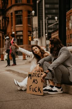 two women sitting on the curb with a sign that says married as fock