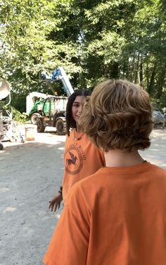 two young boys standing next to each other on a dirt road in front of trees