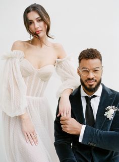 a man in a suit and woman in a white dress posing for the camera with their arms around each other