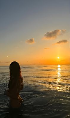 a woman is sitting in the water at sunset