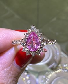 a woman's hand holding a ring with a pink diamond in the middle and white diamonds surrounding it