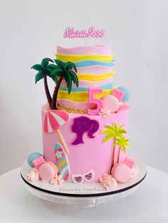 there is a pink cake decorated with palm trees and beach items on the top tier