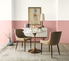 two chairs sitting at a table in front of a pink and white wall with a painting on it