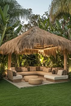 an outdoor living area with grass and palm trees in the background, including a couch under a thatch roof