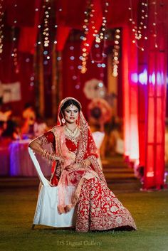 a woman in a red and white wedding dress sitting on a chair with her hands on her hips