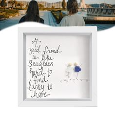 two women sitting in front of a white frame with writing on it