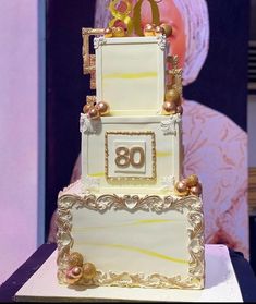 a three tiered cake with gold decorations on top and the number 80 on it