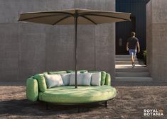 a green couch with pillows and an umbrella in front of a concrete building that has stairs leading up to it