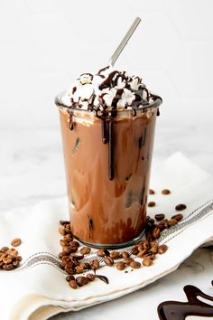 a glass filled with chocolate and whipped cream on top of coffee beans next to a spoon