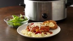 a white plate topped with meat covered in sauce and rice next to a crock pot