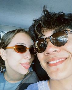 two people are taking a selfie in the back seat of a car, one is wearing sunglasses