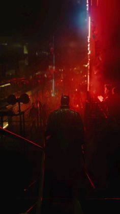 the dark knight stands in front of red and blue lights at night, with his back turned to the camera