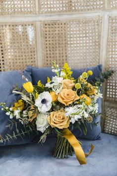 a bouquet of yellow and white flowers sitting on top of a blue couch next to a pillow